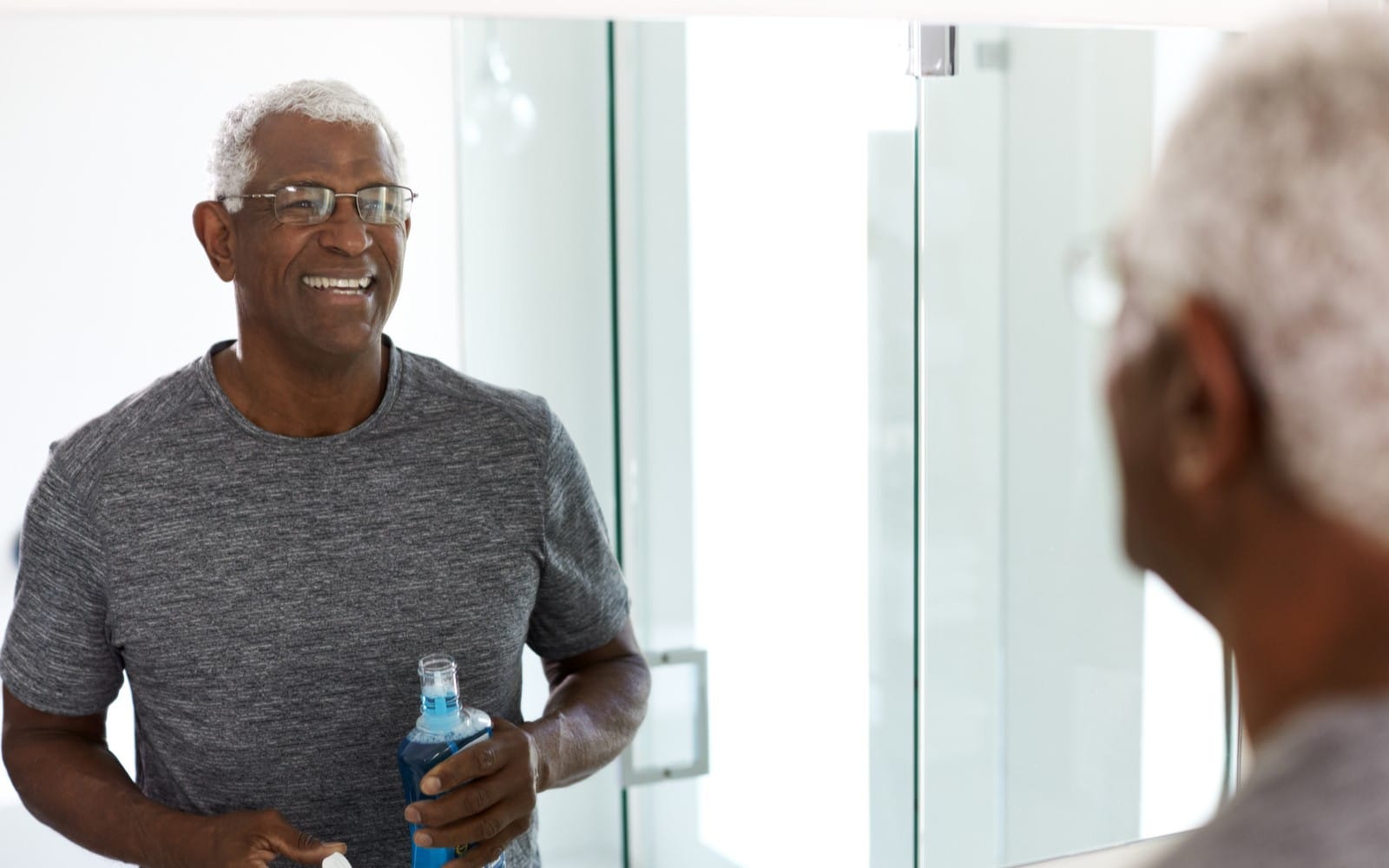 senior man using mouthwash looking at reflection